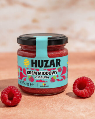 Krem miodowy z maliną HUZAR 250 g w szklanym słoiku, na różowym tle ze świeżymi malinami.